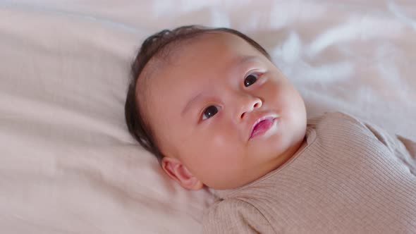 An Asian newborn baby is laying down on a soft white sheet mattress