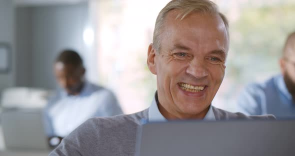 Portrait of Mean Man Sitting at Desk in Office Looking at Laptop Screen and Laughing