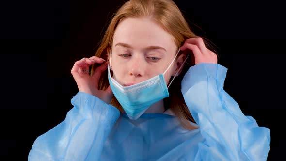 Serious Female Doctor in a Blue Medical Coat Put on a Medical Mask Looking at Camera