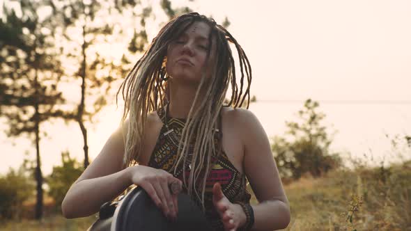 Beautiful Young Hippie Woman with Dreadlocks Playing on Djembe