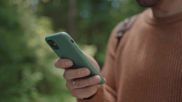 Closeup of a Mobile Phone in the Hands of a Male Traveler Walking Through the Forest