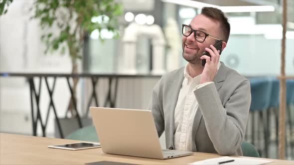 Creative Man with Laptop Talking on Smartphone