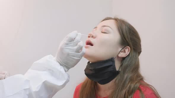 Anonymous doctor putting a cotton stick into nostril of an asian girl for laboratory COVID-19