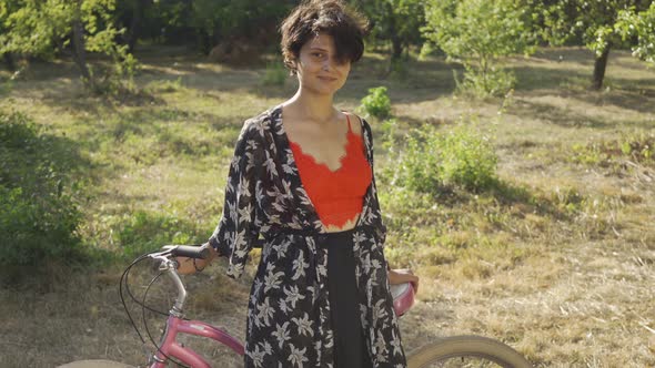 Portrait Cute Young Woman with Short Black Hair Standing in the Garden or Park with Her Bicycle