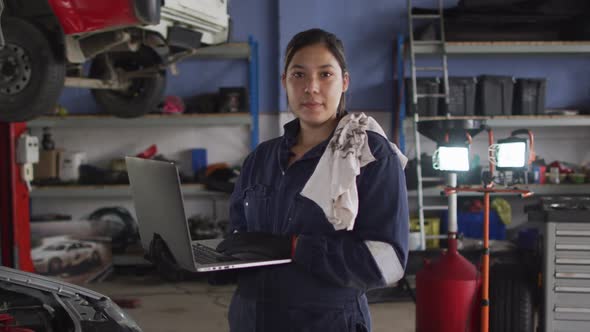 Portrait of female mechanic using laptop and smiling at a car service station