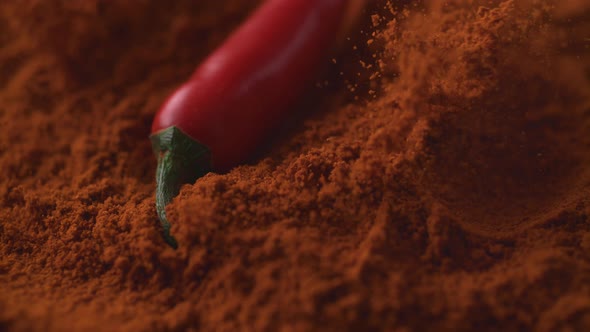 Red chili pepper falling on chili powder. Slow Motion.