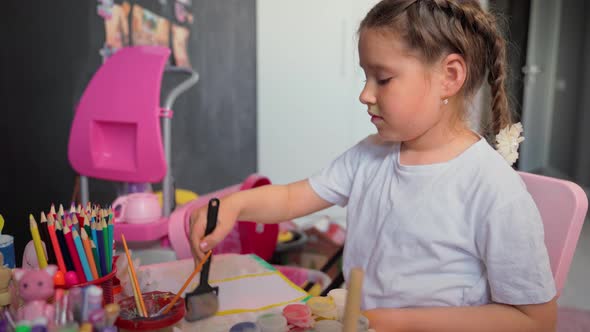 Little girl paints a picture at home. Attractive child female 10s draw with brushes and paints