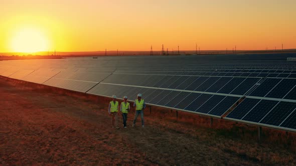 Aerial Zoom Out Shot of Workers Walking About Solar Farm at Sunset