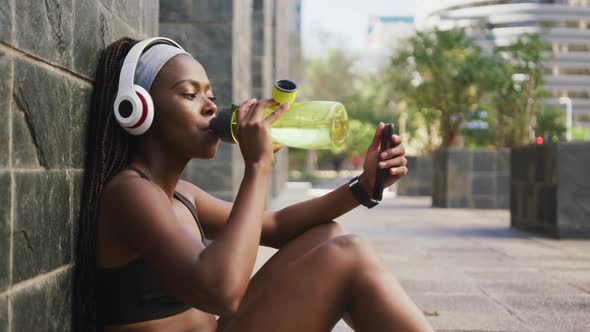 African american woman exercising outdoors drinking water and using smartphone in the city