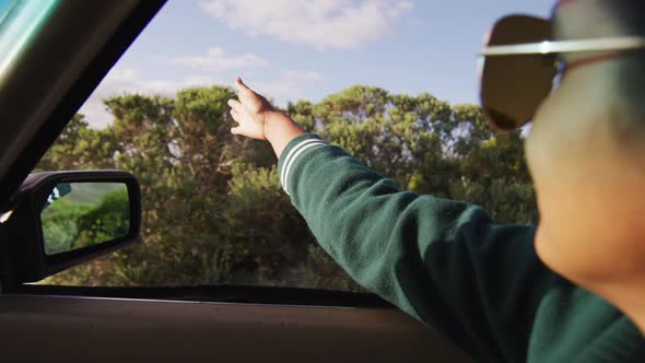 Mixed race woman driving on sunny day in convertible car waving arm and smiling