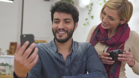 Happy couple with phone making video call in cafe