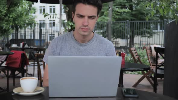 Yawning Tired Man Using Laptop in Cafe Terrace