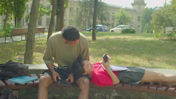 Cheerful Multiracial Couple of Students Relaxing on Bench After Study