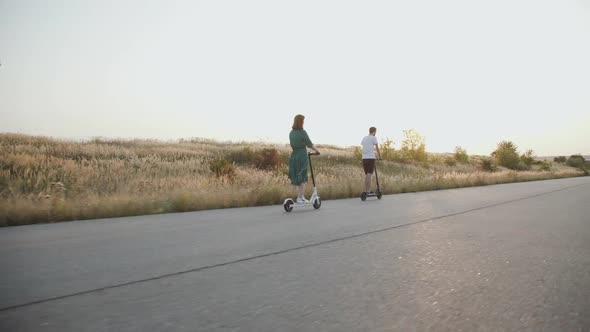 Couple in Love Riding Fast to Sunset on Electric Scooters with Joy on a Road