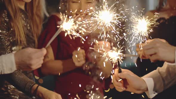 Close-up of Hands Holding and Waving Sparklers. Portraits of Young Caucasian and Asian Girl at