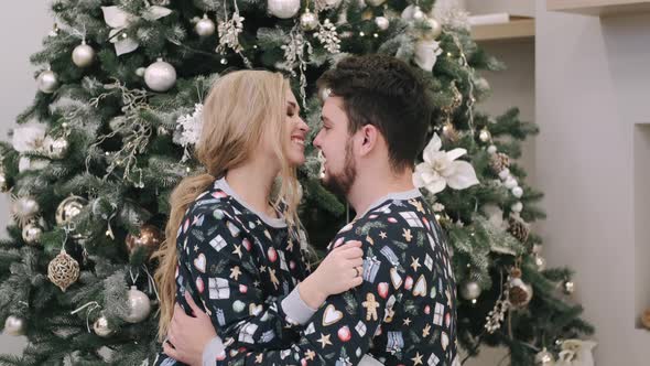 Attractive Cheerful Man and Woman Sitting Near Christmas Tree Hugging