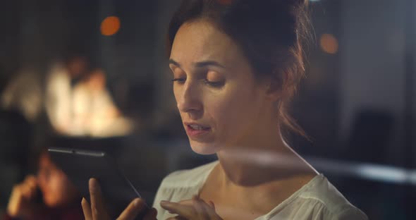 Young Smiling Woman Working Online on Mobile Phone in Office at Night