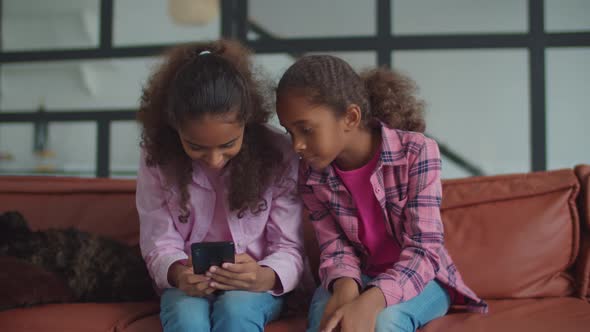 Adorable Black Little Girls Sharing Phone on Couch