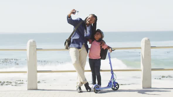 Video of happy african american father and son with scooter taking selfie on promenade