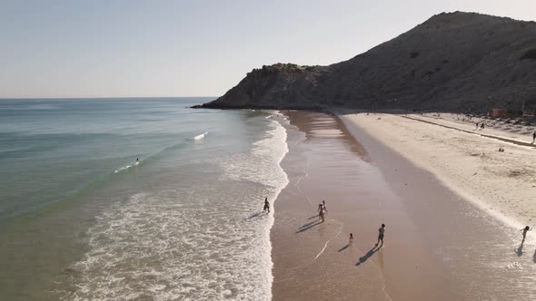People playing at Burgau beach, Algarve, kissed by soft sun light. Aerial pullback