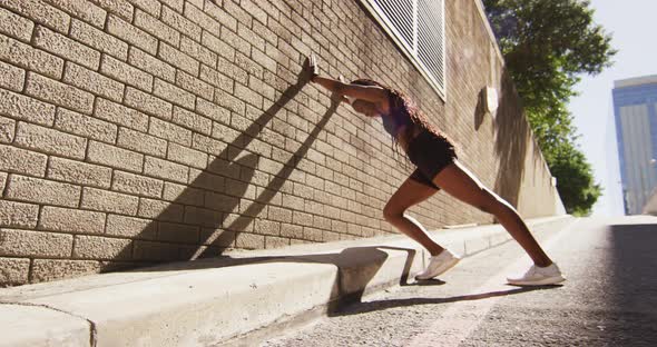 African american woman exercising outdoors leaning of wall and stretching in the city