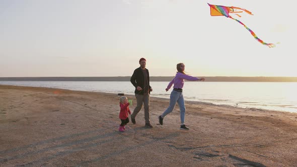 Happy Family Running and Having Some Fun with Flying Kite at the Seashore During Sunset Slow Motion