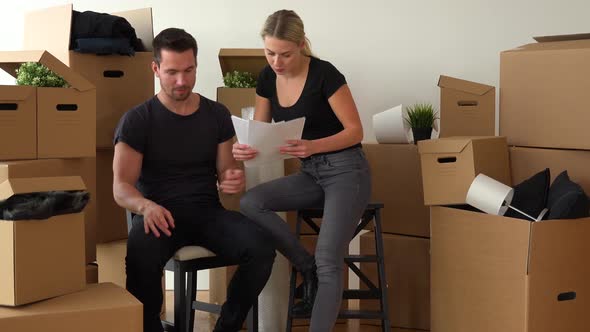 A Moving Couple Sits on Chairs in an Empty Apartment and Checks the List of Possessions