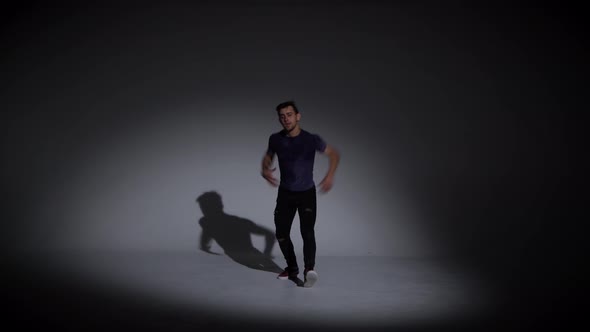 Man Is Dancing Breakdance on the Dark Background in Simple Grey T-shirt and Grey Jeans