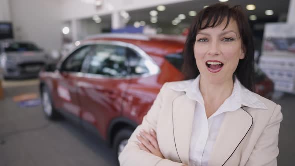 Happy Woman Making Excited Facial Expression Standing on the Right with Blurred Red New Car at