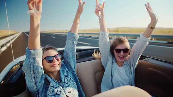 Girls in Back Seat of Convertible Raises Her Hands Up Holding Glasses of Champagne. Women in