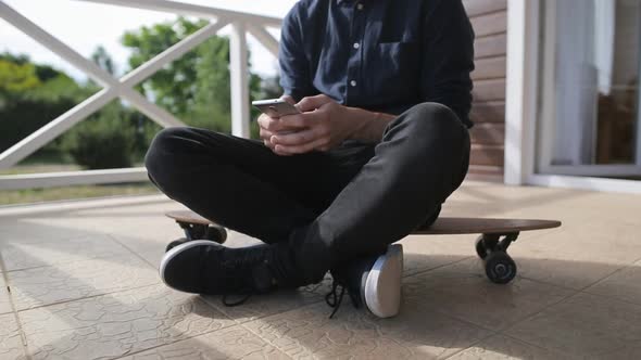 Young man using a smartphone while sitting at longboard on terrace of house