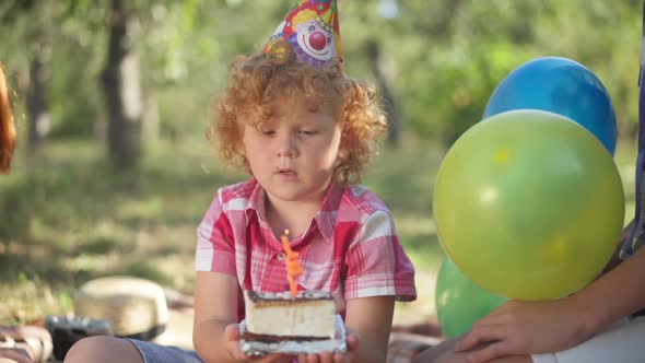 Portrait of Charming Little Redhead Caucasian Boy in Party Hat Blowing Candle on Birthday Cake