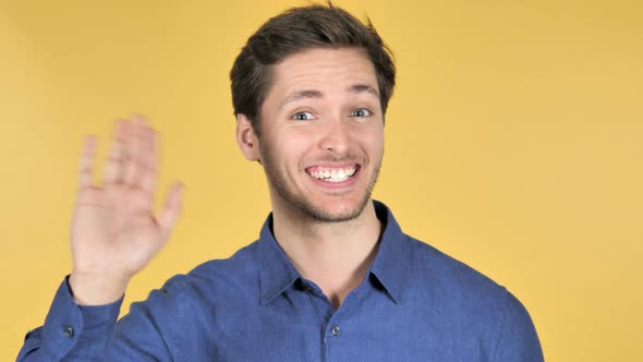 Casual Young Man Waving Hand to Welcome on Yellow Background