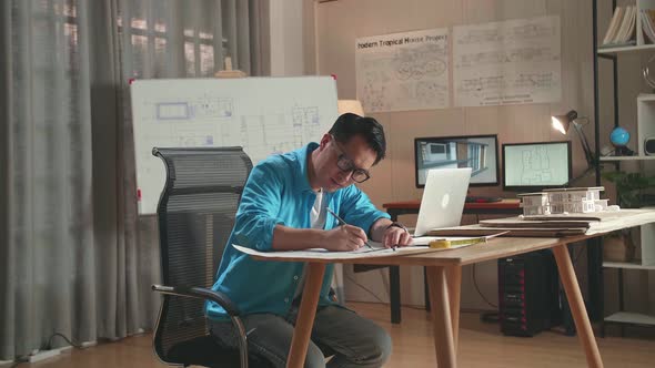 Asian Man Engineer With A Laptop Drawing Blueprint At The Office