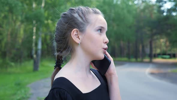 Teen Girl Stands on Park Road and Talks on Phone Closeup