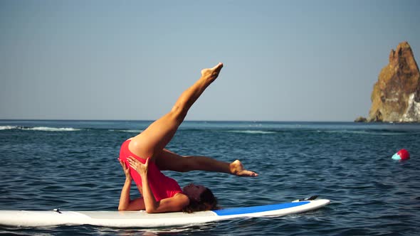 Young Woman in Red Swimsuite Doing Yoga or Pilates on Sup Board with Paddle