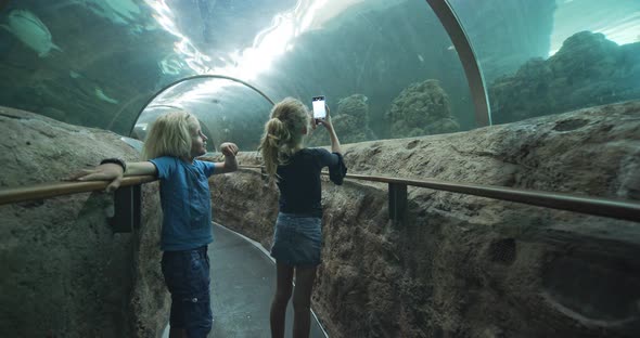 Girl Talking Photos with Little Brother in Glass Tunnel in Oceanarium