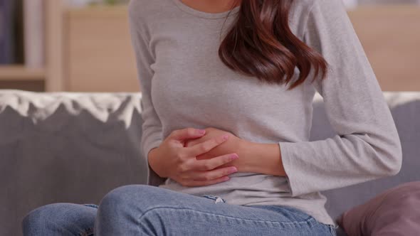 A long hair woman sitting on the couch and always squeeze on her belly