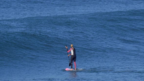 A woman rides an sup stand up paddleboard while surfing on a pink surfboard.