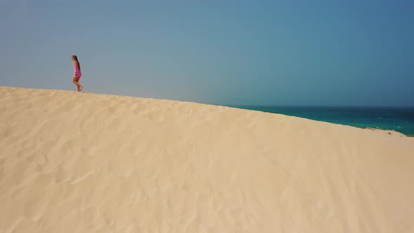 Aerial Adorable Girl Walking Among the Dunes in the Desert at Natural Park Corralejo