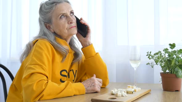 Beautiful Old Grandmother with Grey Hair and Face with Wrinkles is Using Smartphone Talking with