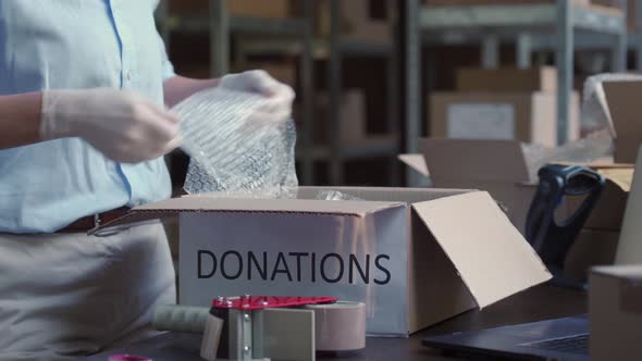 Female Warehouse Worker Wearing Mask Packing Donations Box Closeup