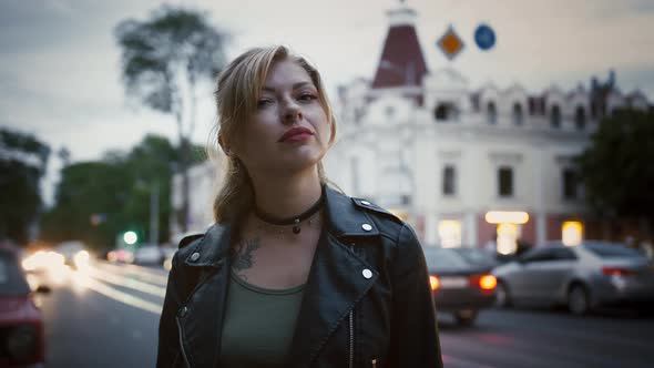 Young Female Hipster in Black Leather Jacket and Choker is Posing Against a Road of City Street with