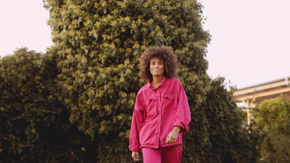 Smiling Young Woman With Afro Hair In Pink Clothes Walking