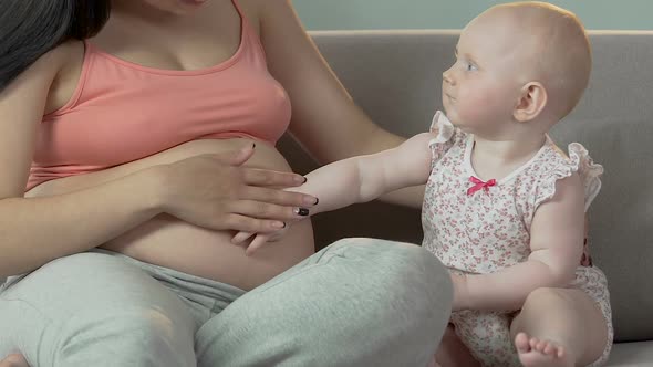 Toddler and expecting female sitting on sofa, child touching belly with hand