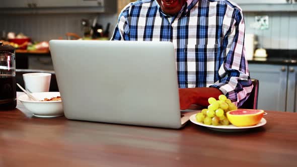 Smiling senior man using laptop while having breakfast