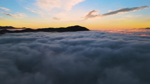 Aerial View of Vibrant Sunrise Over White Dense Clouds with Distant Dark Mountains on Horizon