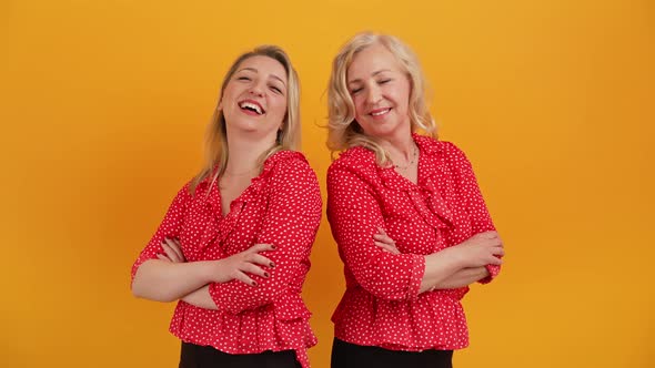 Two Attractive Cheerful Women in Their 40s in Similar Outfits Standing Back to Back with Their Arms