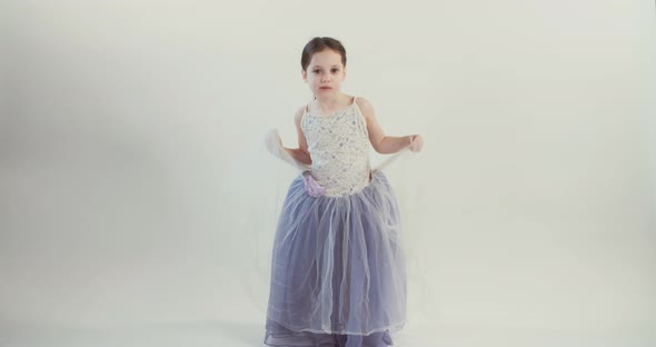 Little girl wearing a dress dances on a white studio background