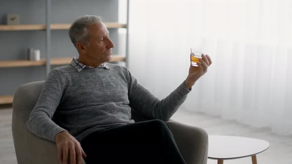 Senior Man Drinking Whiskey While Relaxing in Armchair at Home